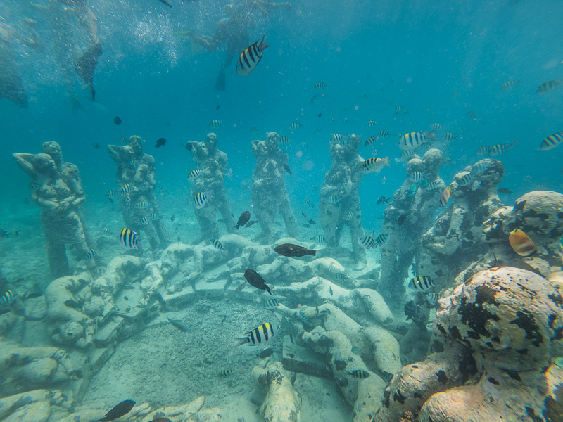 Statues on the seabed with several fishes swimming around